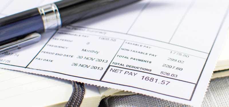 A close-up of a pay stub with a pen lying on top of it.