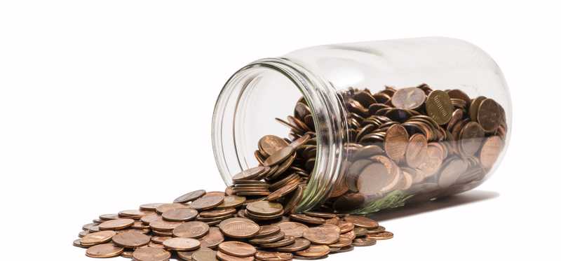 A glass jar tipped over with pennies spilling out.