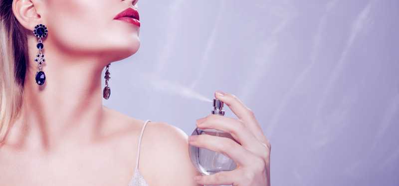 A woman sprays herself with perfume.