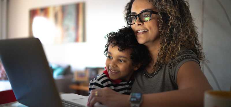 Person at home with child looking at laptop.
