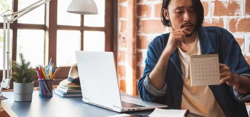 Person pausing from using laptop to study a calendar