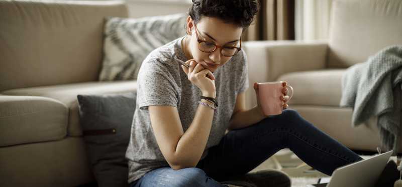 Person sitting on floor looking at documents and laptop.