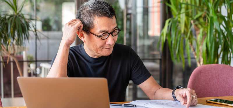 Person with laptop is looking at documents and thinking.