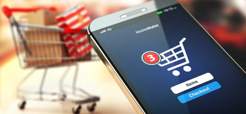A full shopping cart and cell phone being held up for payment.
