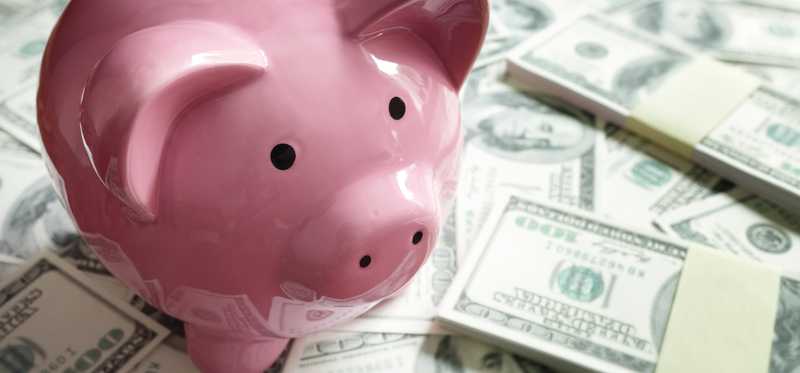 A pink piggy bank sitting on top of a pile of cash.