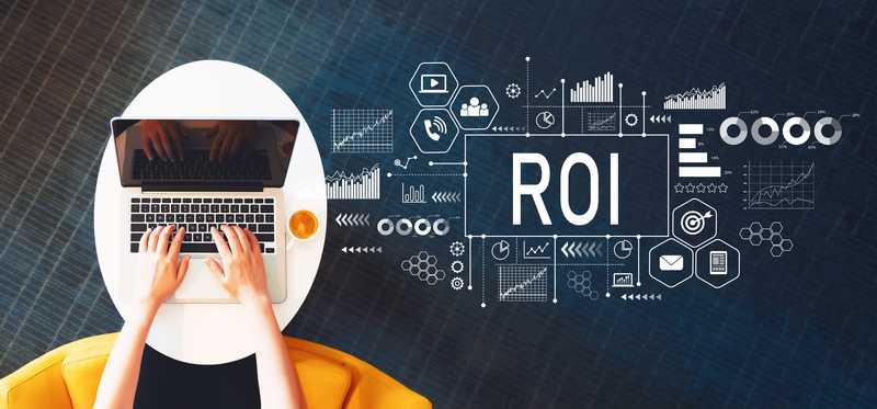 Two hands typing on laptop near charts and the letters ROI.
