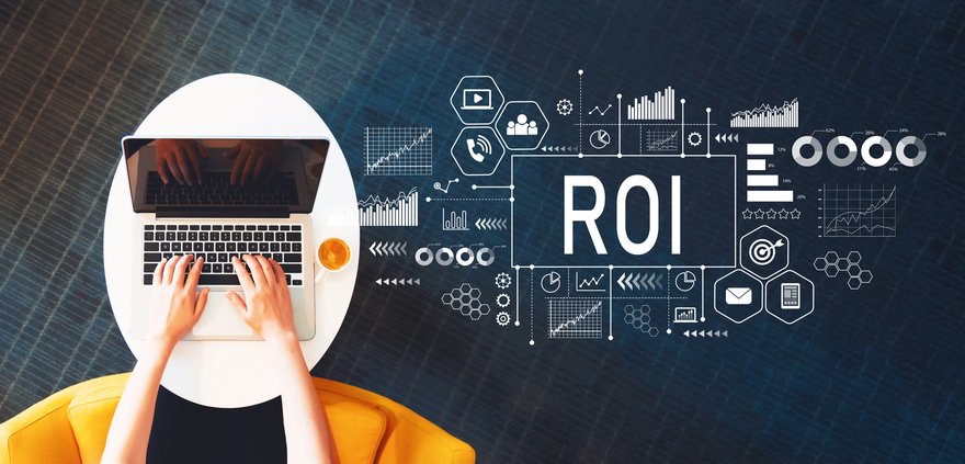 Two hands typing on laptop near charts and the letters ROI.