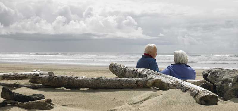 An elderly couple sits together on the beach.