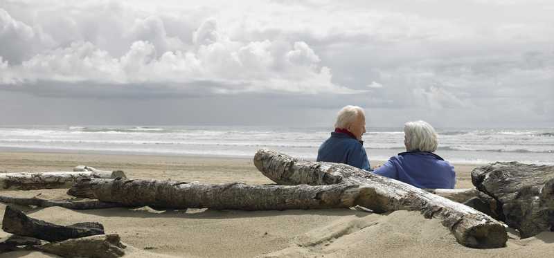 Two people on a beach are sitting in the sand on a cloudy day.