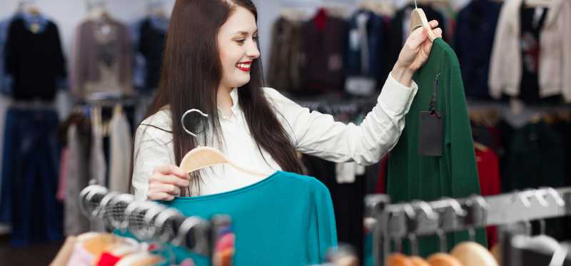 A customer shops for sweaters off a rack.