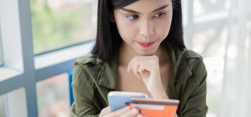 Person holding a phone and credit card while looking thoughtful.