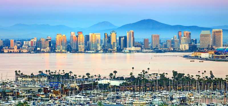 A scenic view of the San Diego, California, skyline with the ocean and a marina with many boats and mountains in the background.