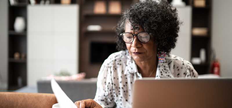 Person reviews paperwork in front of laptop at home with a cup of tea.