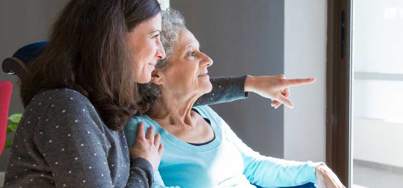 Senior and caregiver looking out window.