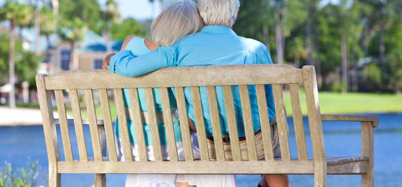 Senior couple sitting together on a bench overlooking a pond.