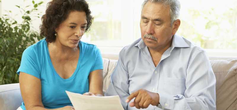 Two people sitting on couch and pointing at document.