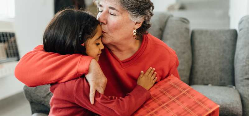 Adult holding present and kissing child's forehead.