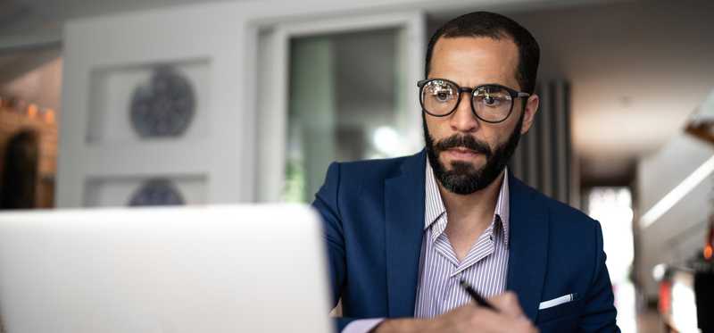 Serious person in glasses staring at laptop and writing note.
