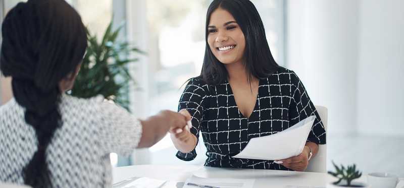 Two people shaking hands over a desk.