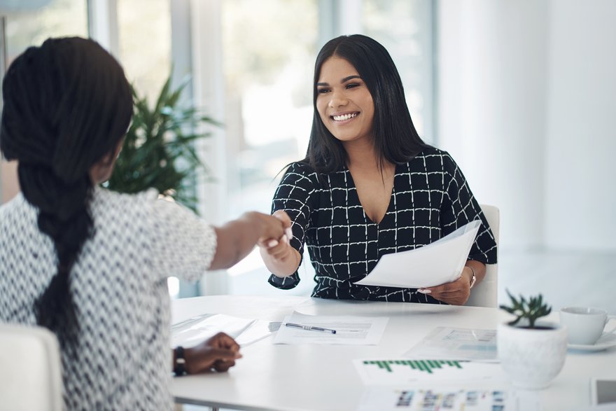 Two people shaking hands over a desk.