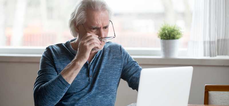 Shocked person taking off glasses and looking at laptop.