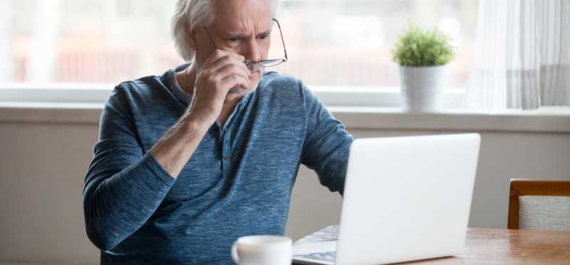 Shocked senior man taking off glasses and looking at laptop