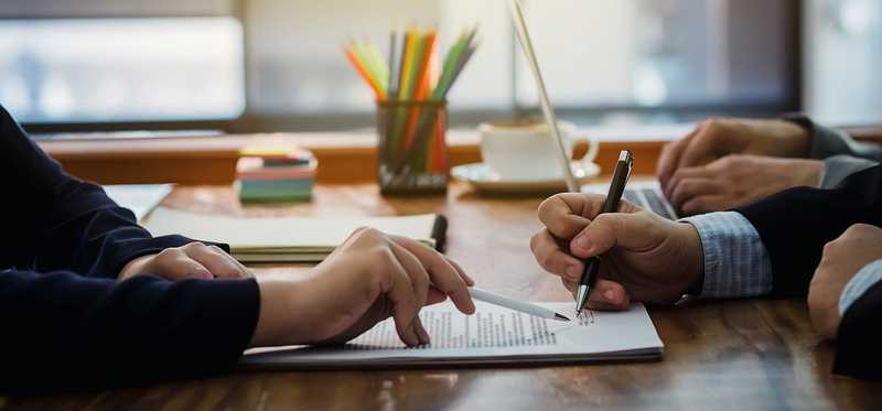 Two sets of hands are shown over a contract while one set signs paperwork.