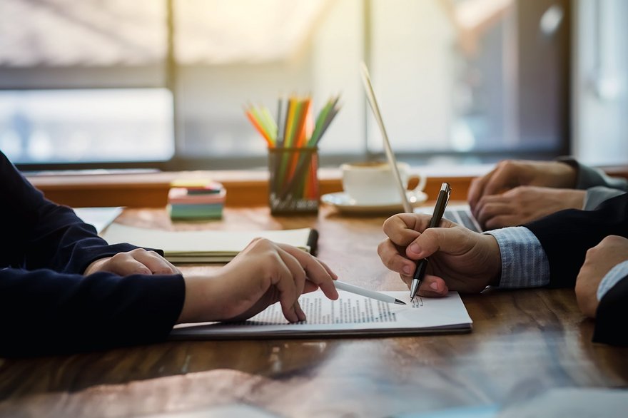 Two sets of hands are shown over a contract while one set signs paperwork.