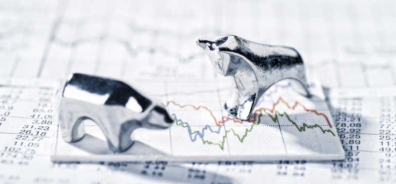 Bull and bear figurine standing on stock chart.