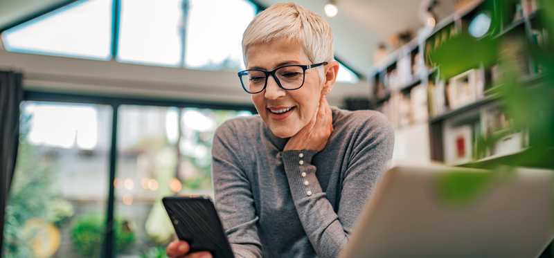 Short-haired woman holding mobile phone and sitting at table with open laptop