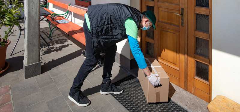 Delivery worker wearing mask and gloves dropping off package at door
