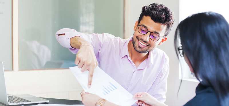 Two people in office looking at paper with bar chart.