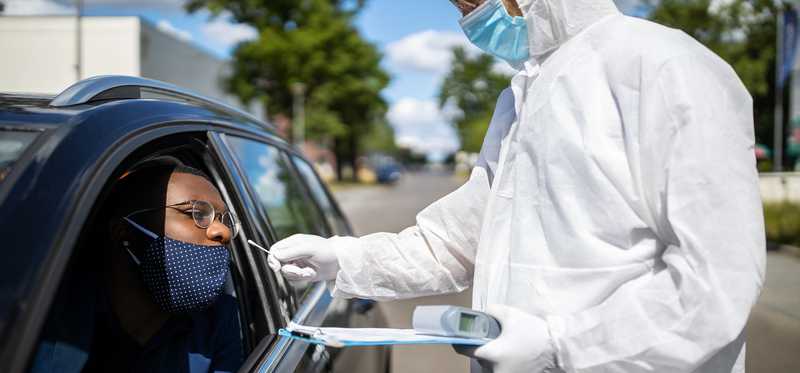 Healthcare worker in personal protective equipment administering coronavirus test at COVID-19 drive-thru test site.