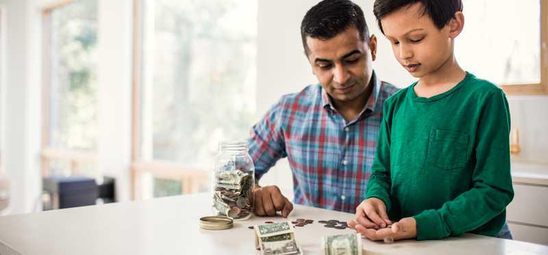 Adult and child counting cash and coins on kitchen counter.