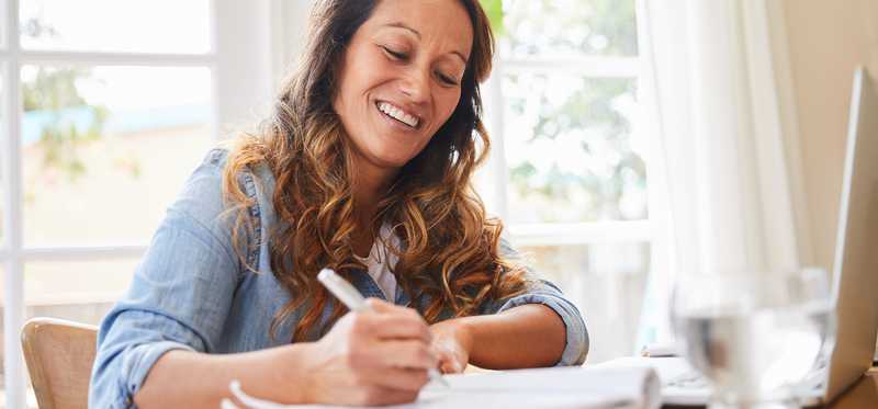 Woman writing in notebook in sunny living room