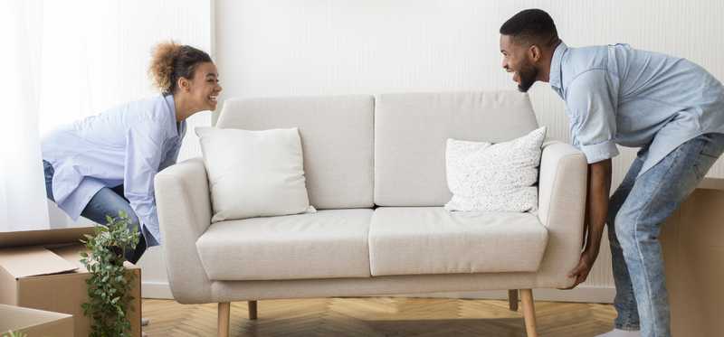 Couple smiling while moving sofa in living room