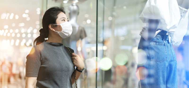 Masked woman standing outside department store window looking at display