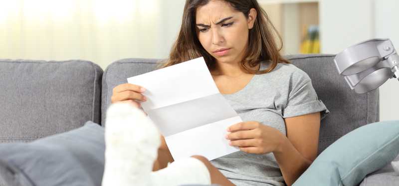 Person with foot in cast looks unhappily at document.