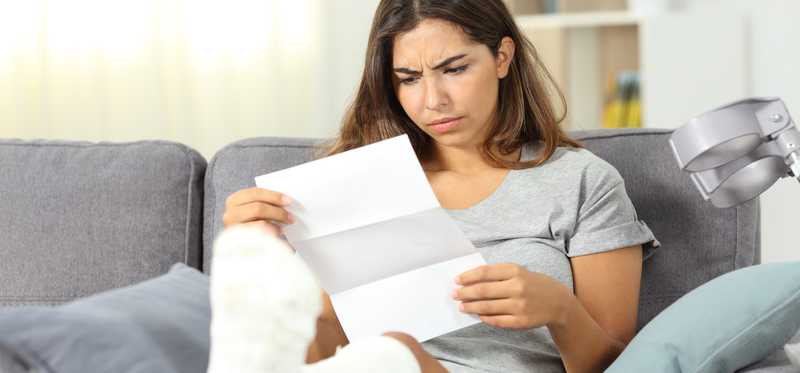 Person with foot in cast looks unhappily at document.