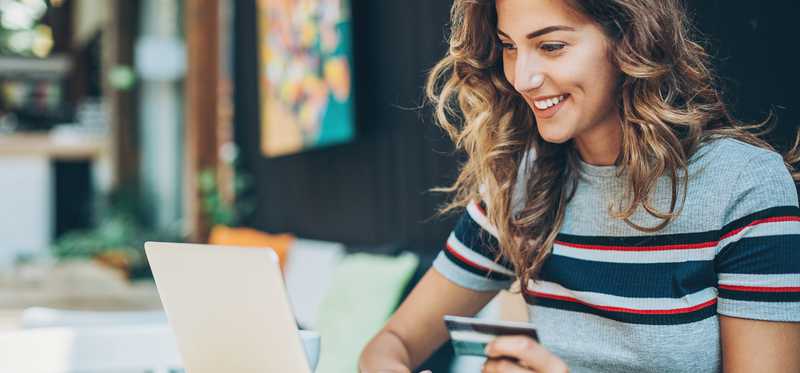 Person smiling while holding credit card and typing on laptop.
