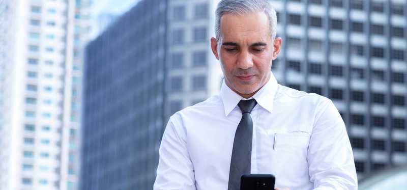 Businessperson standing on balcony in city and looking at mobile device.
