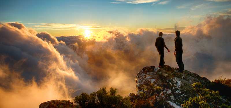 Hikers standing on cliff in the clouds and looking at sunset