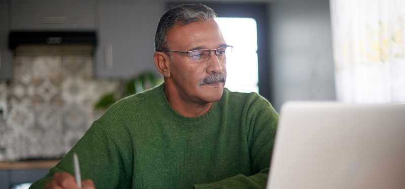 Person writing notes from laptop with coffee cup on desk.