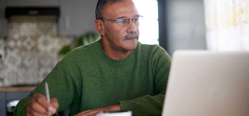 A person looking at a laptop and writing notes.