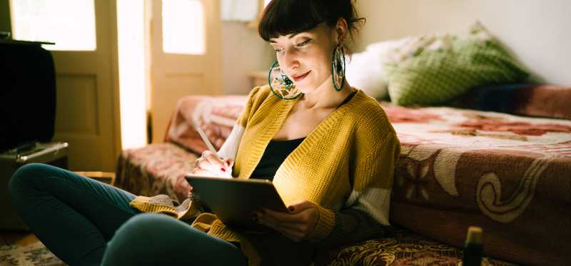 Woman sitting on floor in her dark living room while looking at tablet