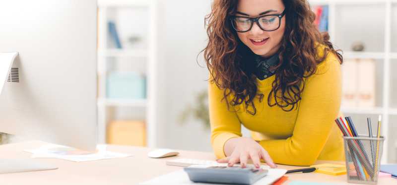 Person smiling while using calculator and reviewing paperwork.