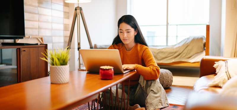 Woman sitting at coffee table in living room and shopping on laptop