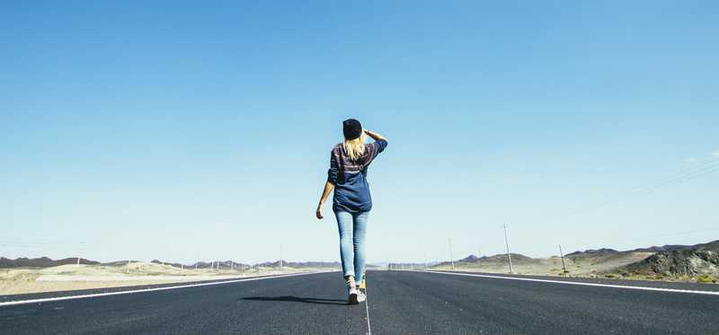 Person standing on open road looking out at distant horizon.