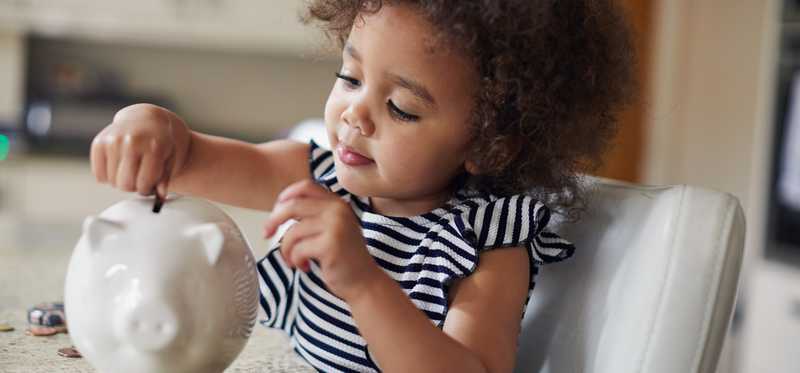 Little girl adding coins to piggy bank