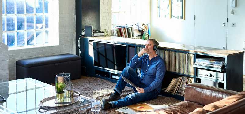 Person sitting on floor of sunny apartment and listening to music through headphones.